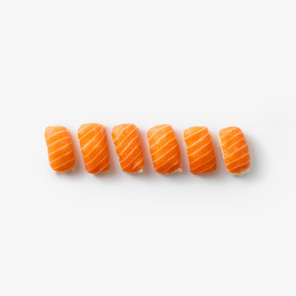 Six pieces of salmon nigiri sushi arranged in a straight line on a white background. Each piece features a slice of orange salmon atop a small bed of white rice.