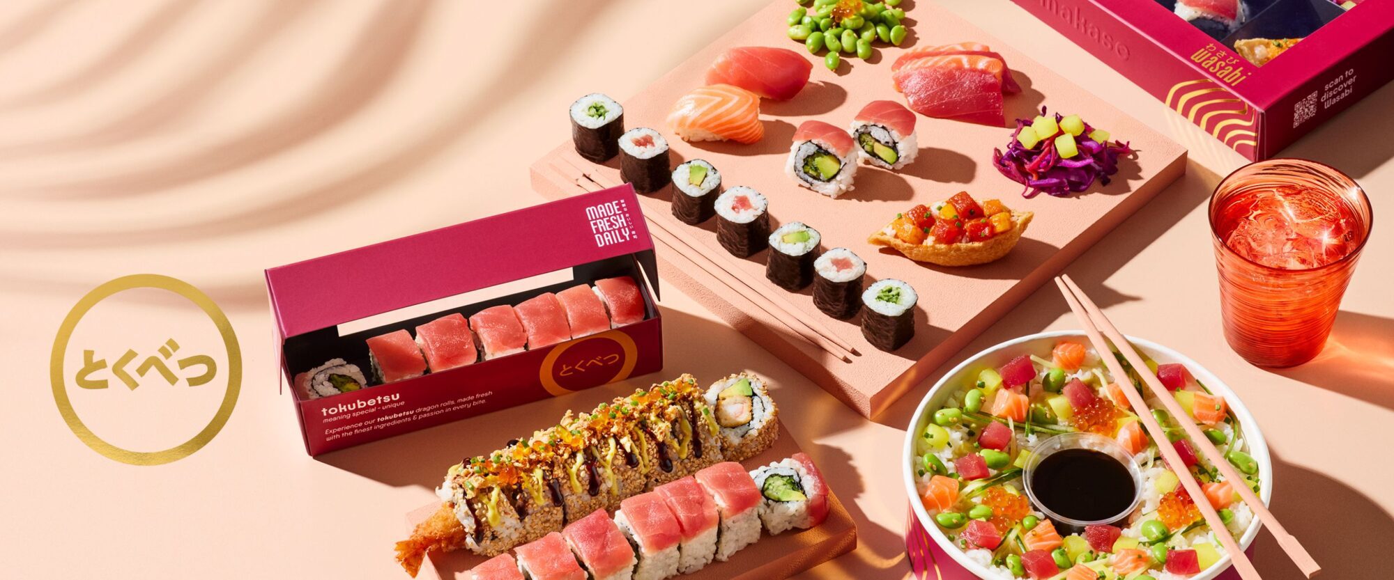 An assortment of sushi rolls, nigiri, and sashimi displayed in colorful boxes and plates, with chopsticks and soy sauce on a peach-colored surface. The word “tokyo” is written in Japanese on the left.