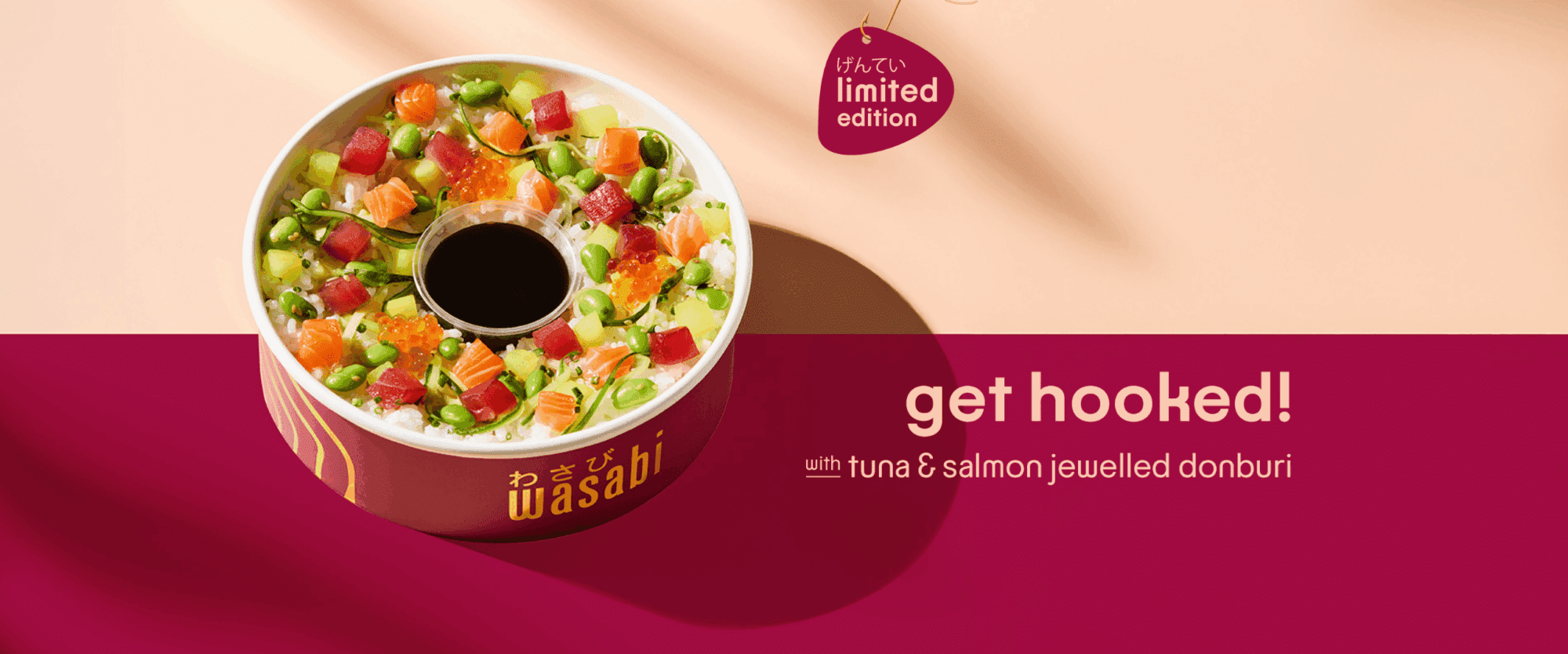A colorful bowl of tuna and salmon jeweled donburi with diced fish, edamame, and roe around a central soy sauce container, on a pink and beige background. Text reads