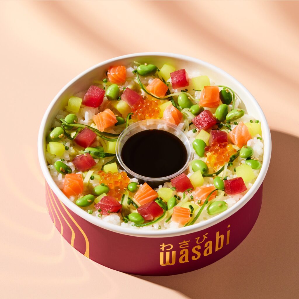 A colorful poke bowl with diced salmon, tuna, edamame, cucumber, and fish roe on rice, arranged around a central soy sauce container. The bowl is labeled 