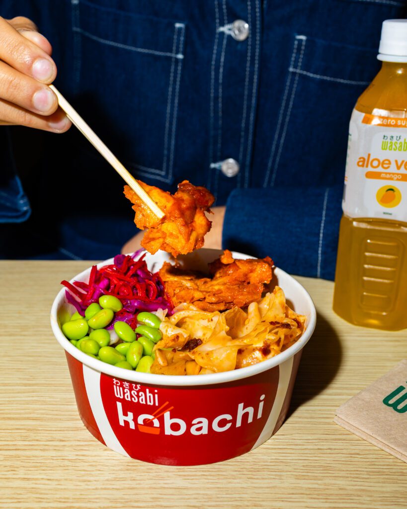 A hand uses chopsticks to pick up food from a bowl labeled