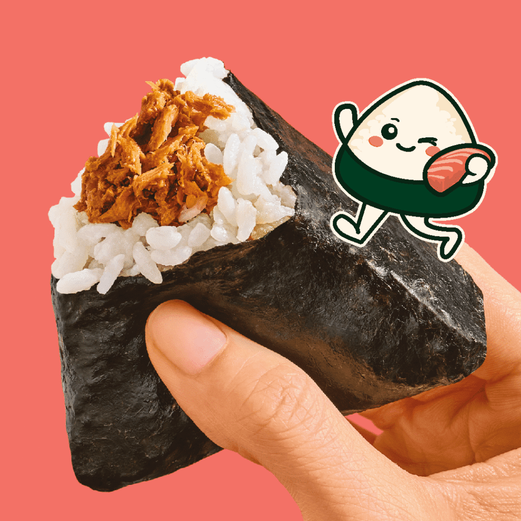 A hand holds a triangular rice ball wrapped in seaweed with shredded filling, next to a cute cartoon rice ball character holding a piece of fish, against a pink background.