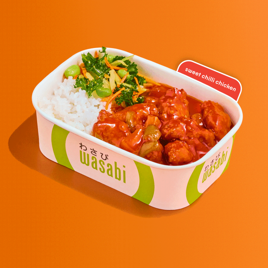 A white and green Wasabi-branded container holds white rice, sweet chilli chicken in sauce, and a side of vegetables on an orange background. A red label reads “sweet chilli chicken.”.